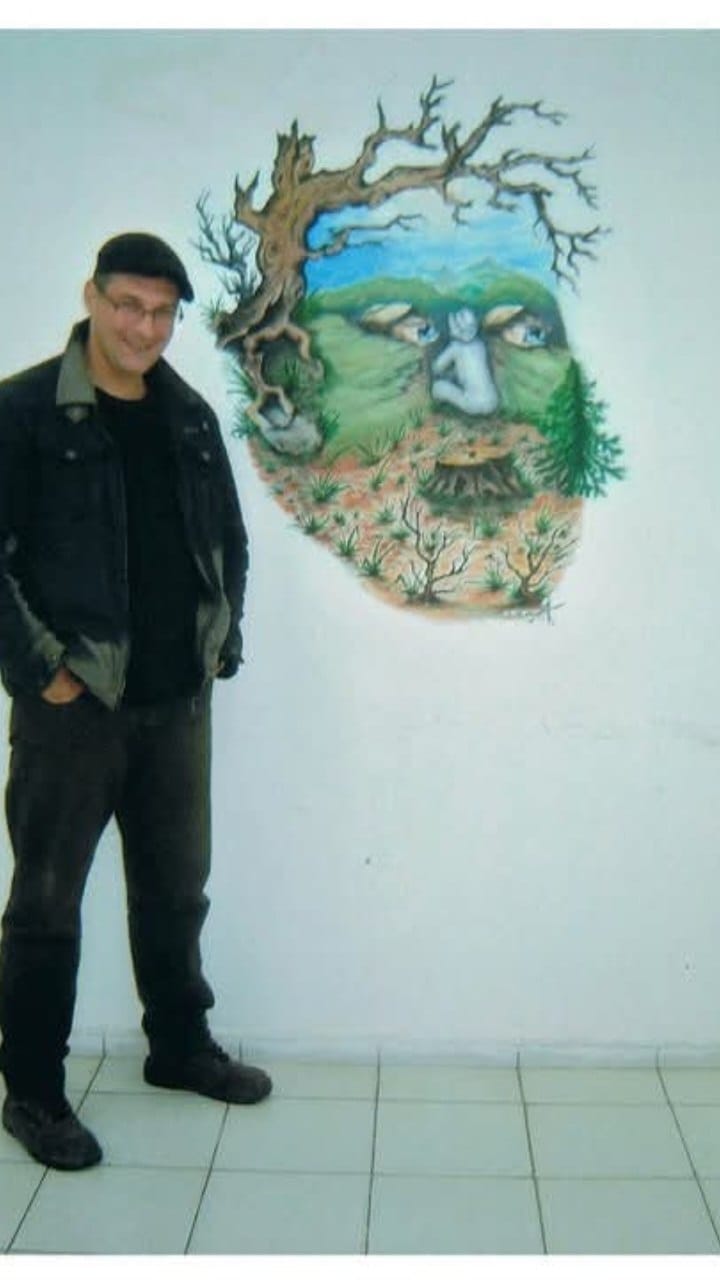 A person stands beside a decorative landscape panel on a white wall.